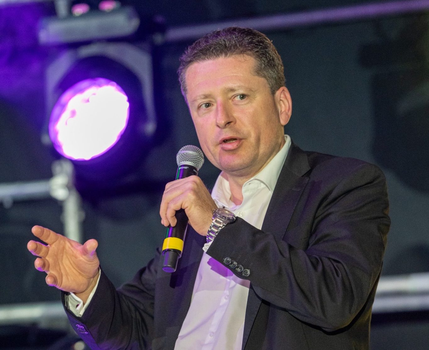 Sascha Höthke hält, mit einem Mikrofon in der Hand, einen Vortrag auf einer Bühne.